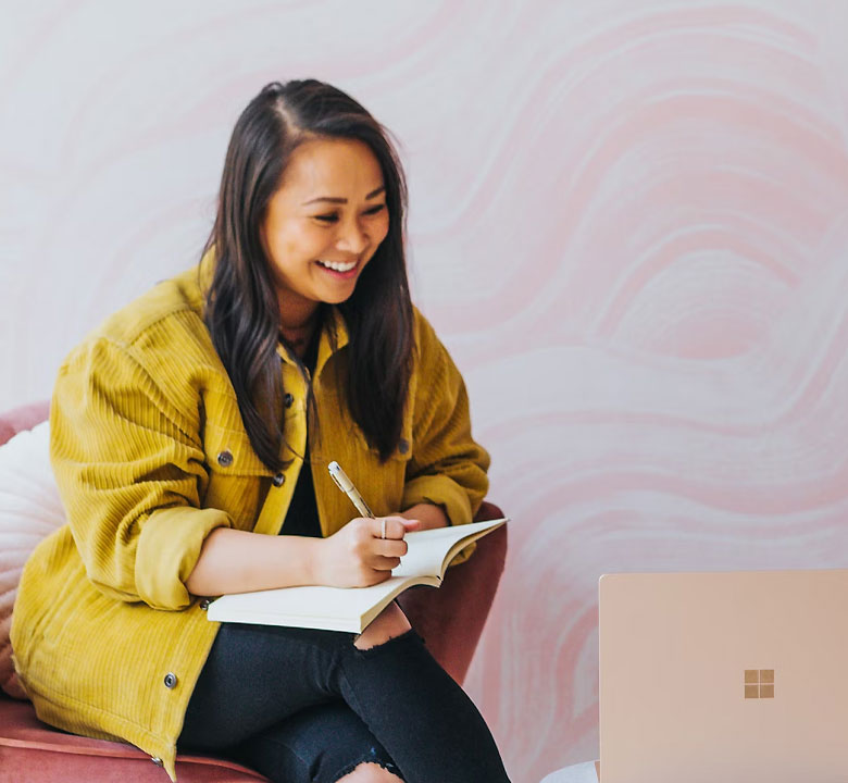 Femme souriante écrivant, assise devant un ordinateur.