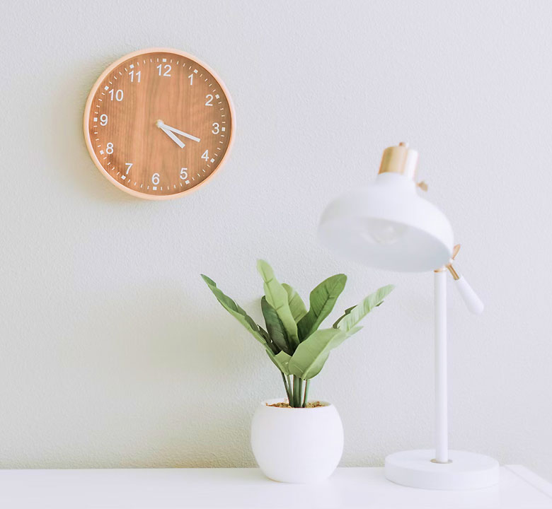 Horloge en bois, plante et lampe blanche.