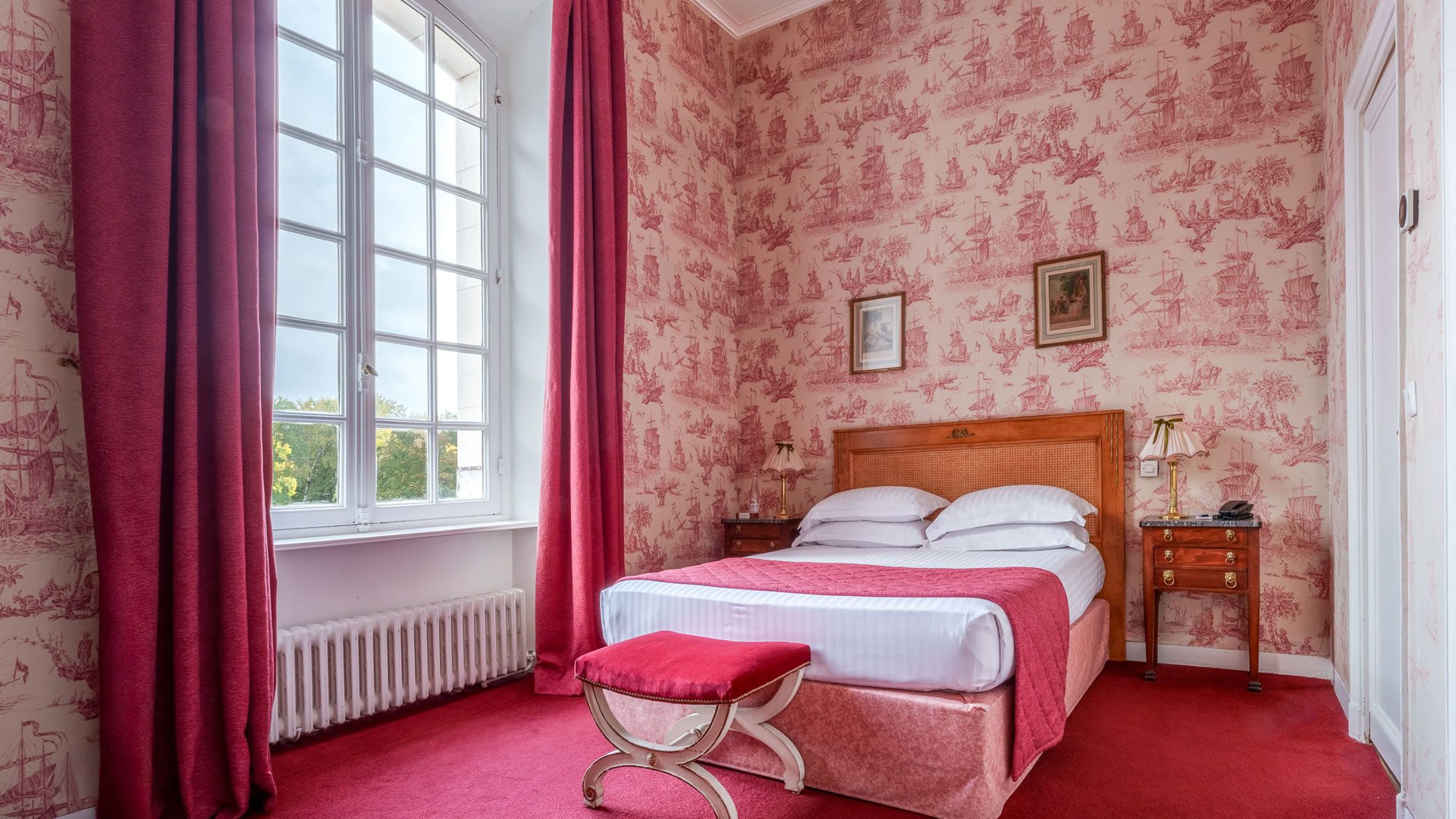 Chambre avec lit, papier peint rouge, fenêtre.